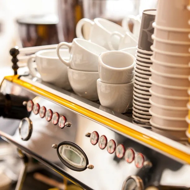 Close-up of the coffee station at Parcafé at The Dorchester, showcasing an espresso machine topped with neatly stacked cups and saucers, ready for barista-crafted drinks.