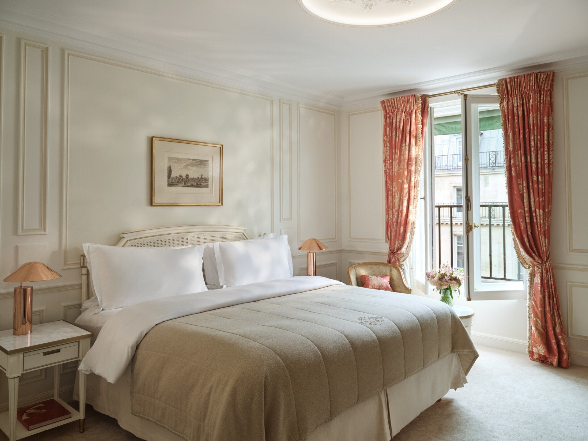 Room of a Pompadour Suite with the bed between two night table and a chair next to a table with flowers on the top, at Le Meurice, Paris