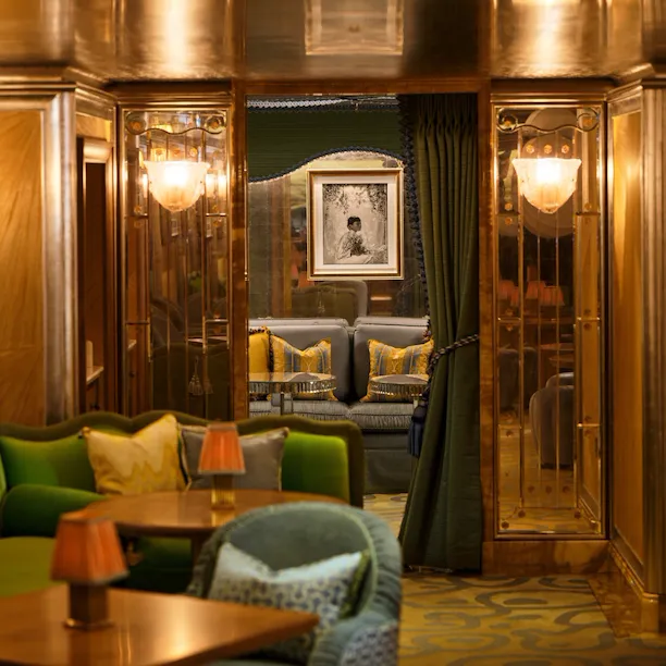 The Snug at The Vesper Bar, a secluded seating area framed by rich wood panelling, green seating and elegant draped curtains.