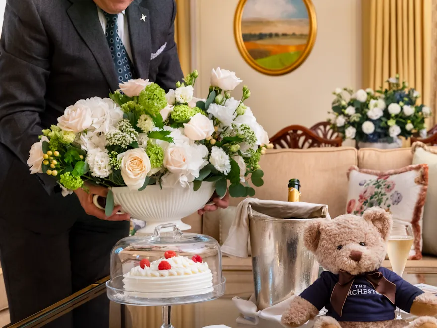 Butler in Dorchester suite with floral arrangement, champagne and Dorchester teddy bear