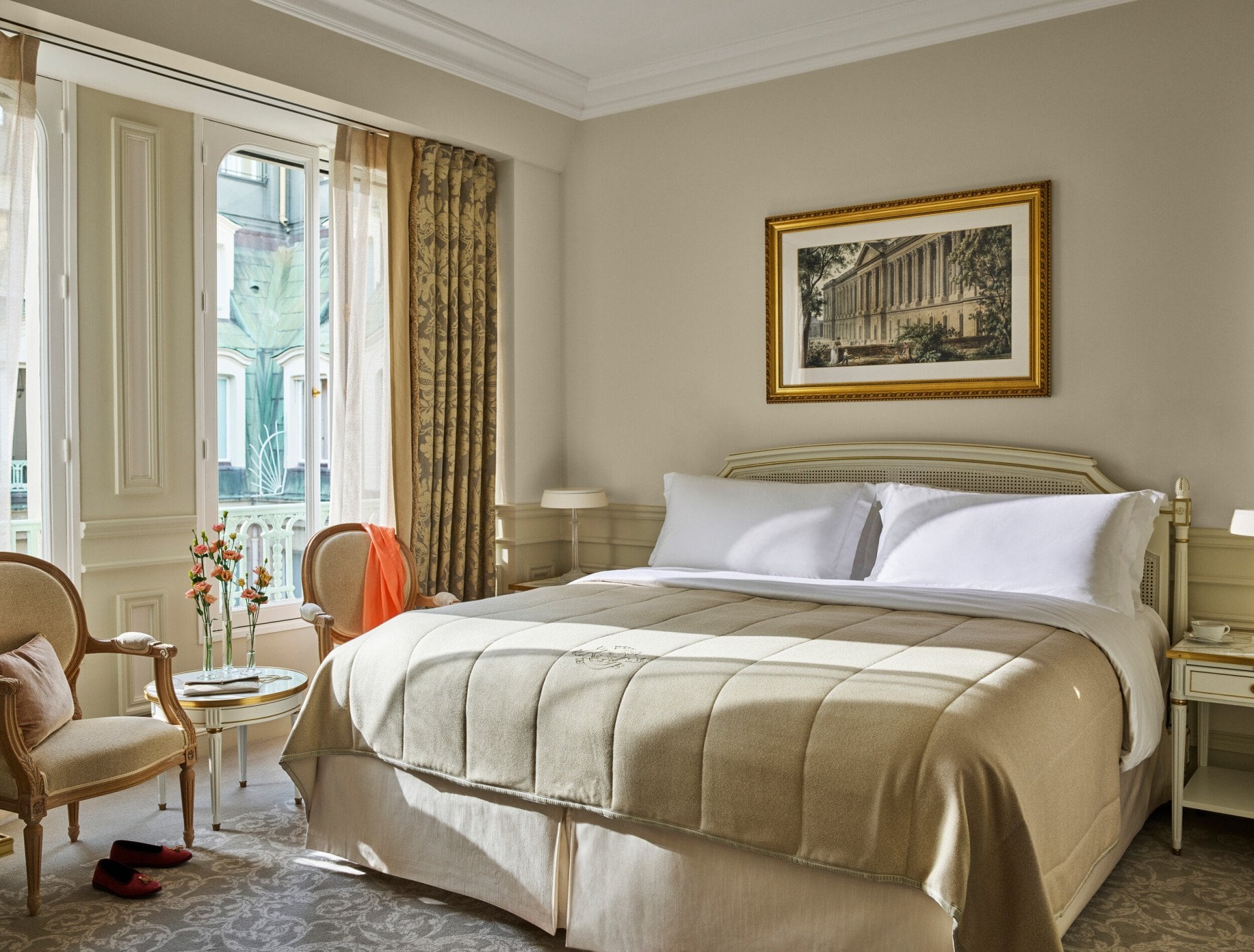 Superior room in beige and white tones with a queen bed and flowers on a low table, at Le Meurice, Paris.