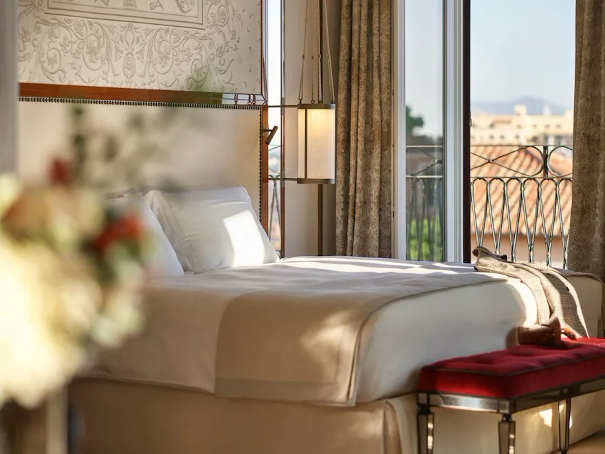Elegant bedroom Presidential Suite, headboard with peacocks decoration and big window with view of Rome at Hotel Eden