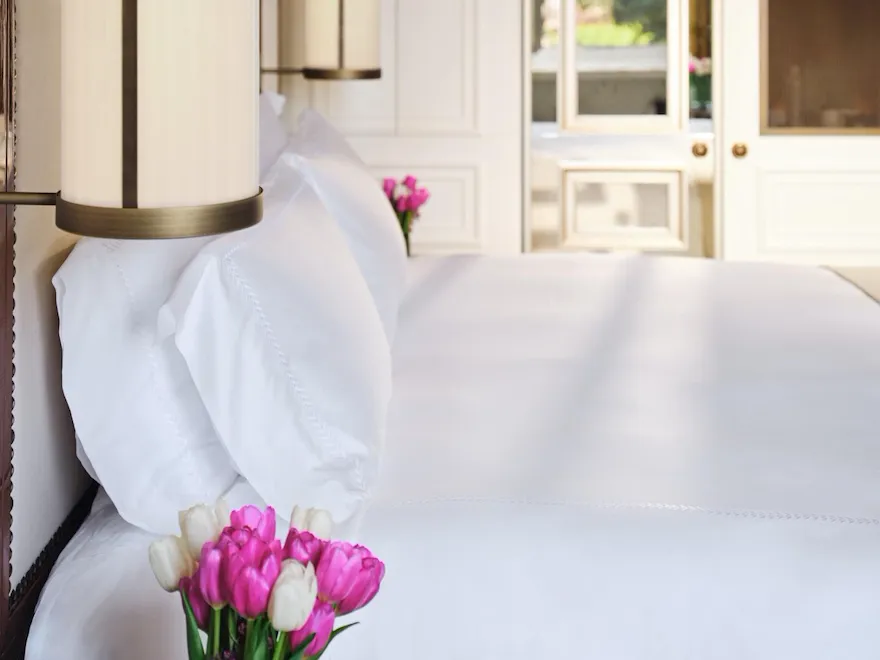 Bedroom detail of freshly made bed with flowers on the sidetable.