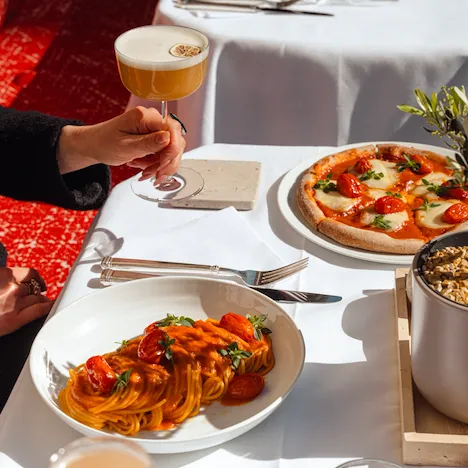 Pasta and pizza on a white table, a hand hold a cocktail.