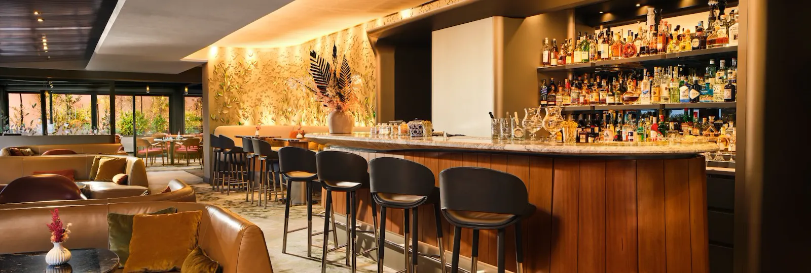 A modern bar with a seating area, illuminated counter, cozy atmosphere, and large windows.