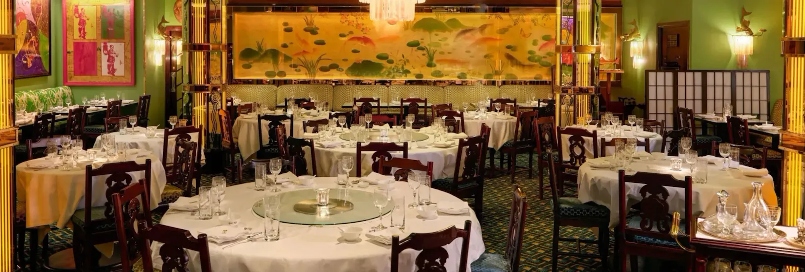 Main dining room at China Tang at The Dorchester, featuring round banquet tables, a statement chandelier and a panoramic Chinese-inspired mural.