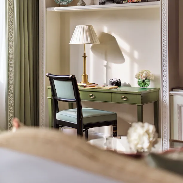 The Executive Park View Room at The Dorchester, showcasing a built-in writing desk with a green leather surface, elegant shelving styled with books and ceramics, and natural light streaming through nearby windows.