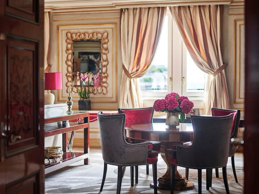 Executive Suite Living Room furnished with a wooden table, four red velvet chairs and a bouquet of pink flowers
