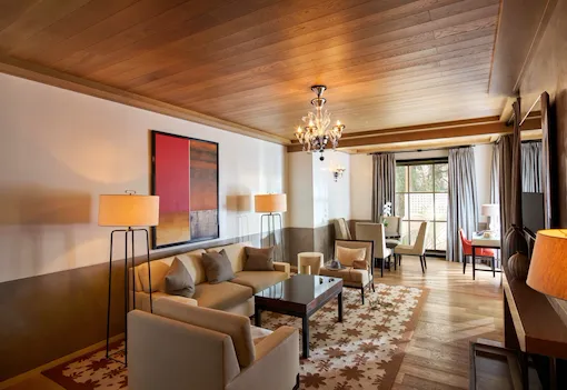 Living room set, artwork, door to private patio, dark and rich colors with pop of reds and elegant chandelier in the Grand Suite at Hotel Bel-Air