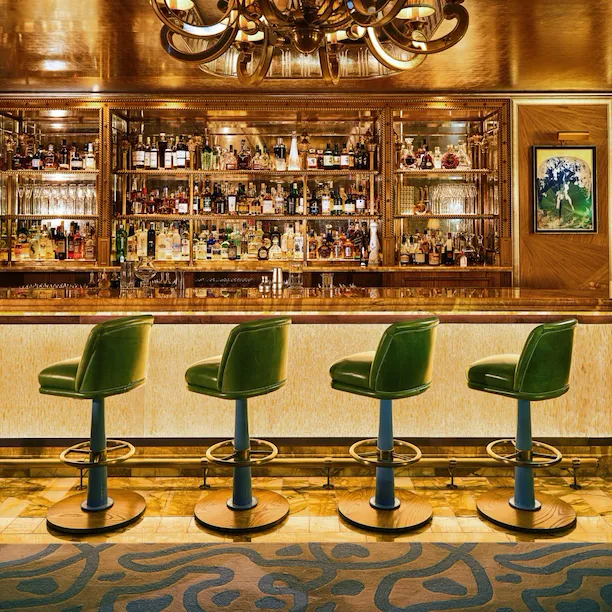 The Vesper Bar at The Dorchester, showcasing a marble bar, green stools, and warm golden interiors.