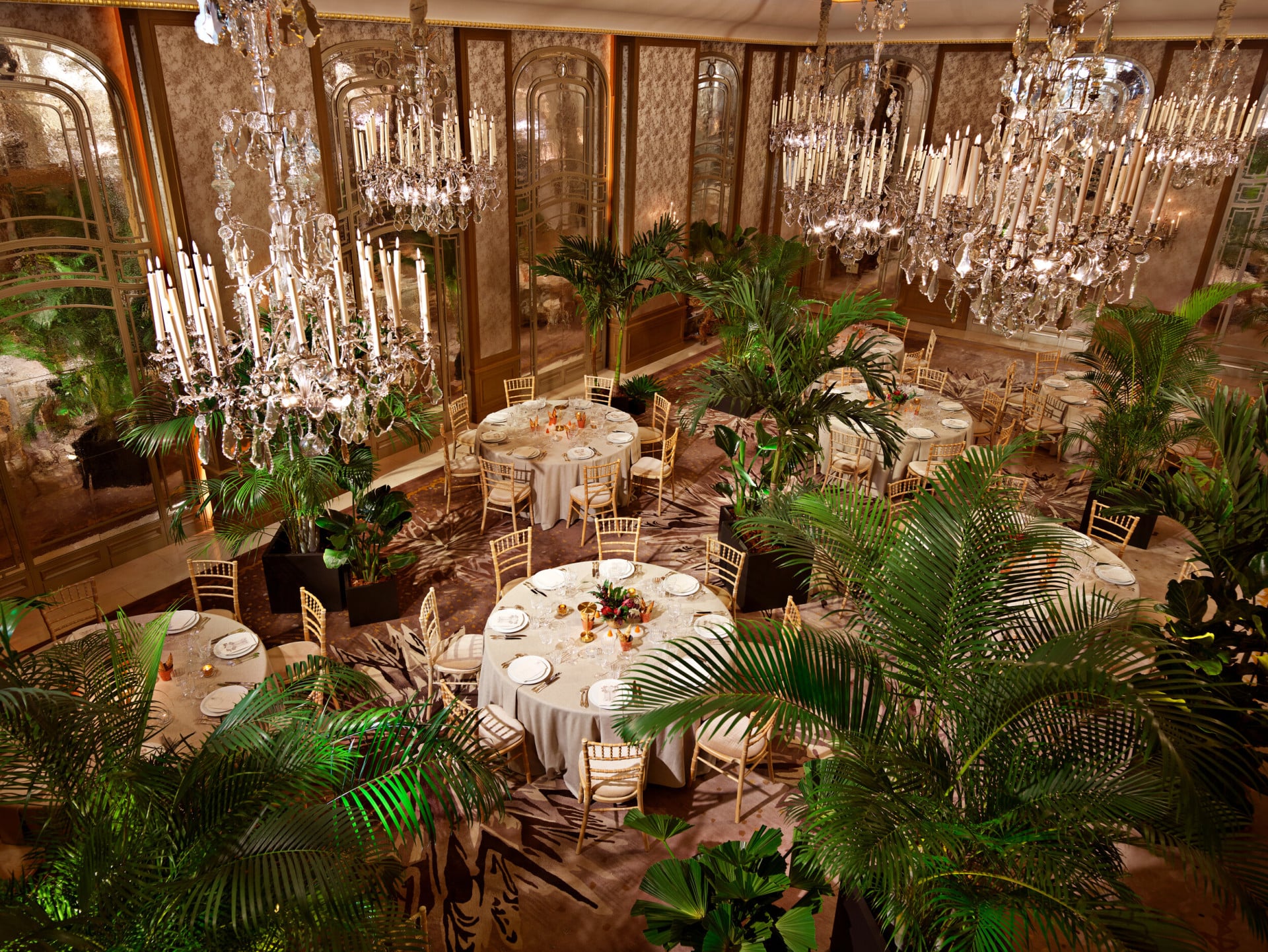 Dinner set up with round tables and palm trees captured in Le Salon Haute Couture, at Hôtel Plaza Athénée, Paris - Dorchester Collection.