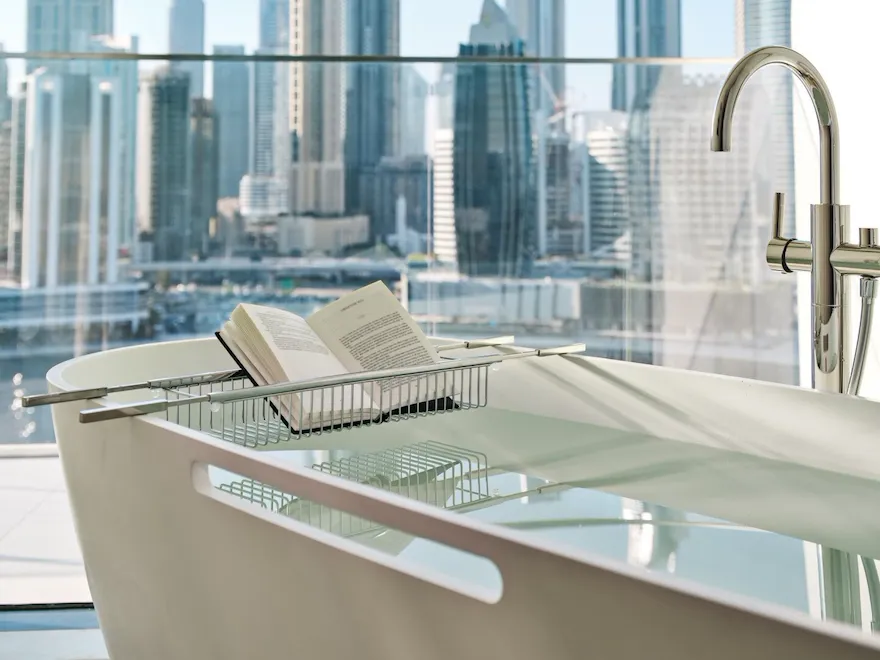 The Suite's bathtub with a book in the stand with Dubai's skyline in the background